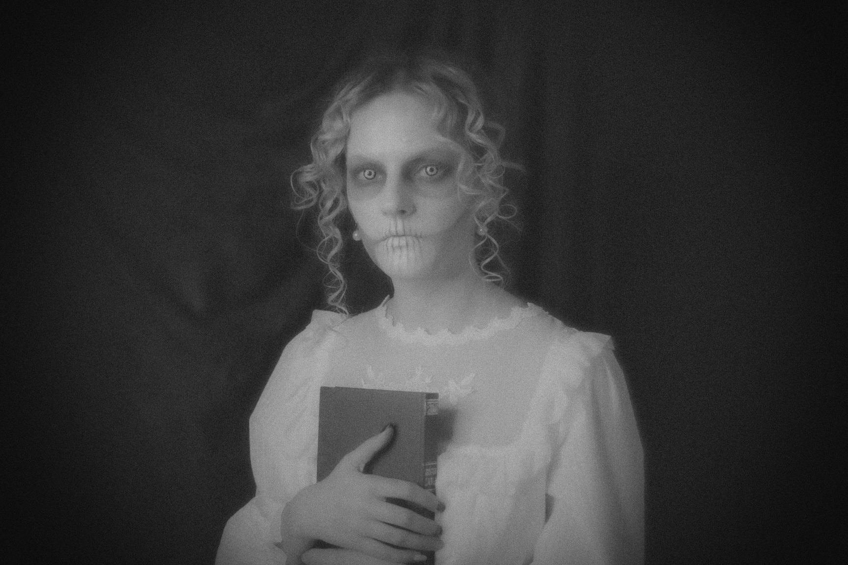 A faded monochrome photo of a white-dressed phantom woman holding a book and staring at the viewer... you.