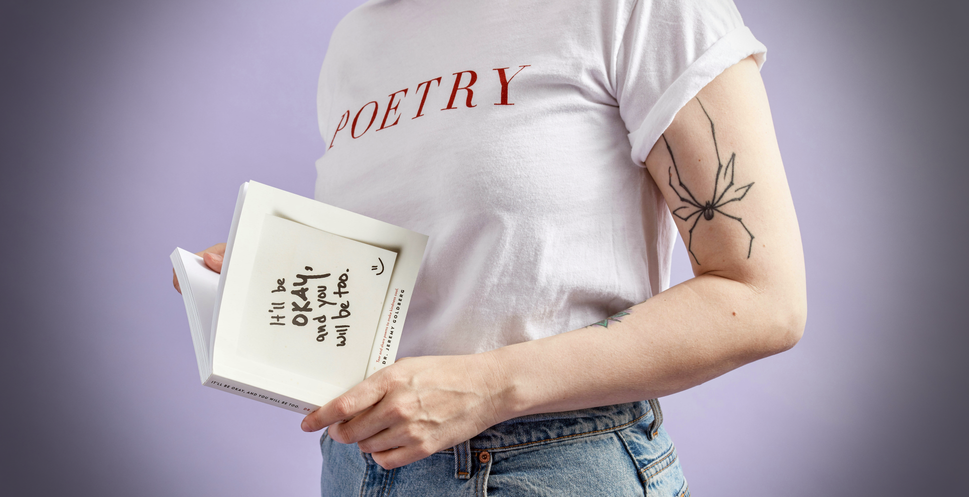 A colour photo of a young woman standing and reading a book. She is wearing a T-shirt showing the word 'Poetry' in bold red capital letters. Photo credit: Thought Catalog on Unsplash.