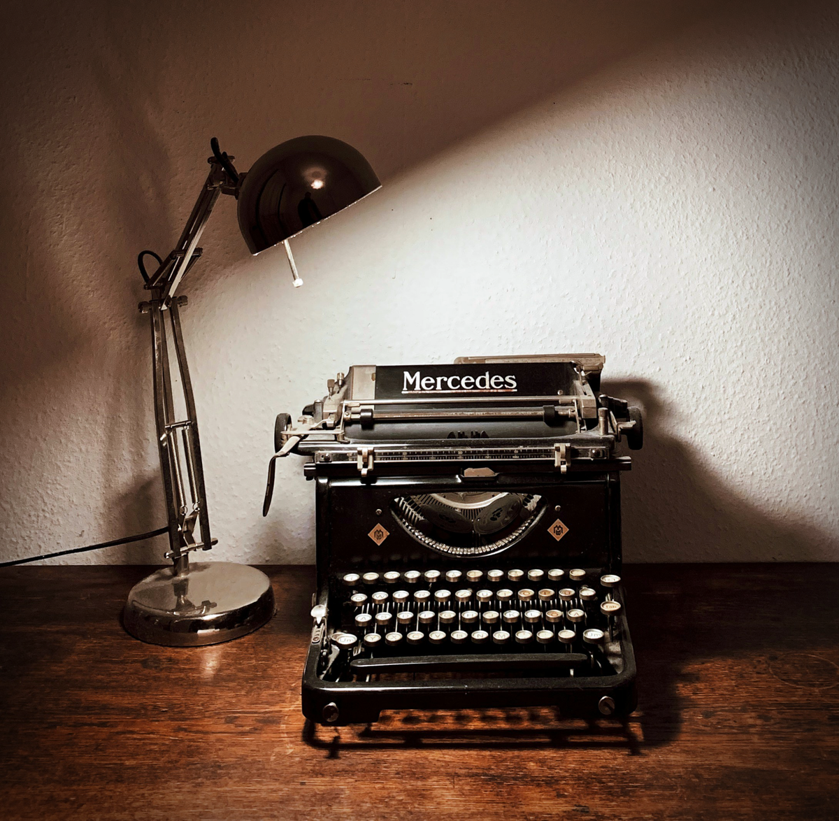 A colour photo of a vintage Mercedes manual typewriter, lit from above by an Anglepoise desk lamp. Image credit: Yusuf Evli from Unsplash.